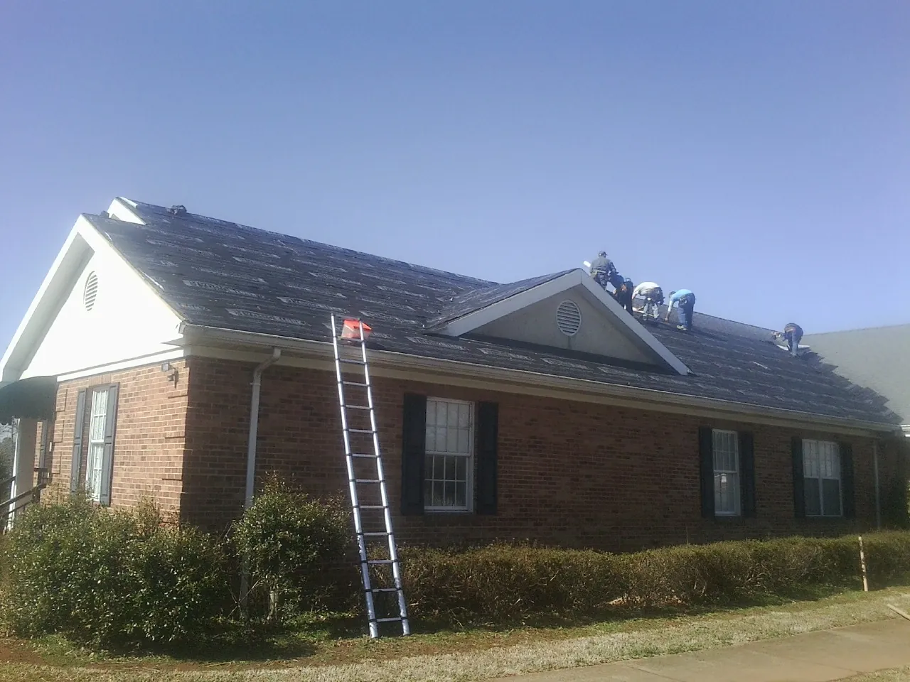 Crew tearing shingles off a brick ranch roof with a ladder set — Emergency Roof Repair work by our crew in Northfield