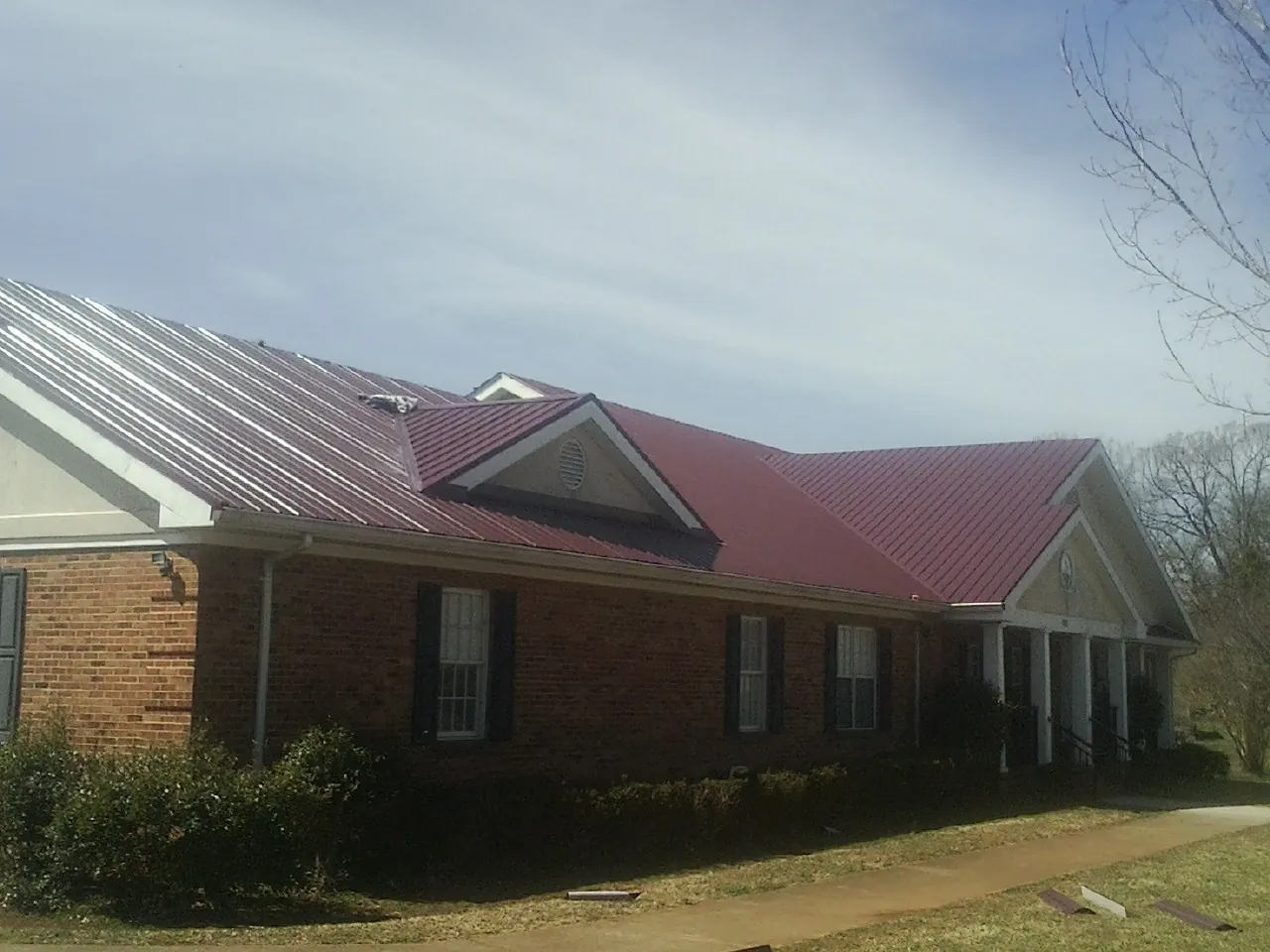 Red metal roof with gabled entries on a long brick building, from a Hail Damage Roof Repair job in Northfield