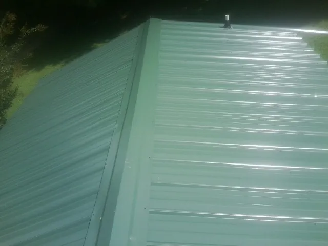 New green metal panels meeting at the ridge of a roof — Flat Roof Repair work by our crew in Northfield