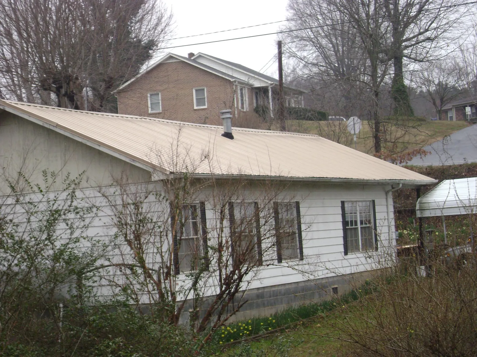 Tan metal roof on a white sided house set into a hillside — Commercial Roofing by Roofing Brothers in Northfield